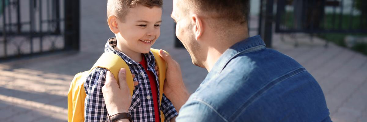 adult man helping young son or child put on school backpack properly, backpack safety concept