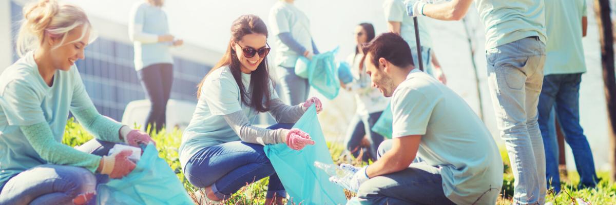 volunteering, charity, cleaning, people and ecology concept - group of happy volunteers with garbage bags cleaning area in park