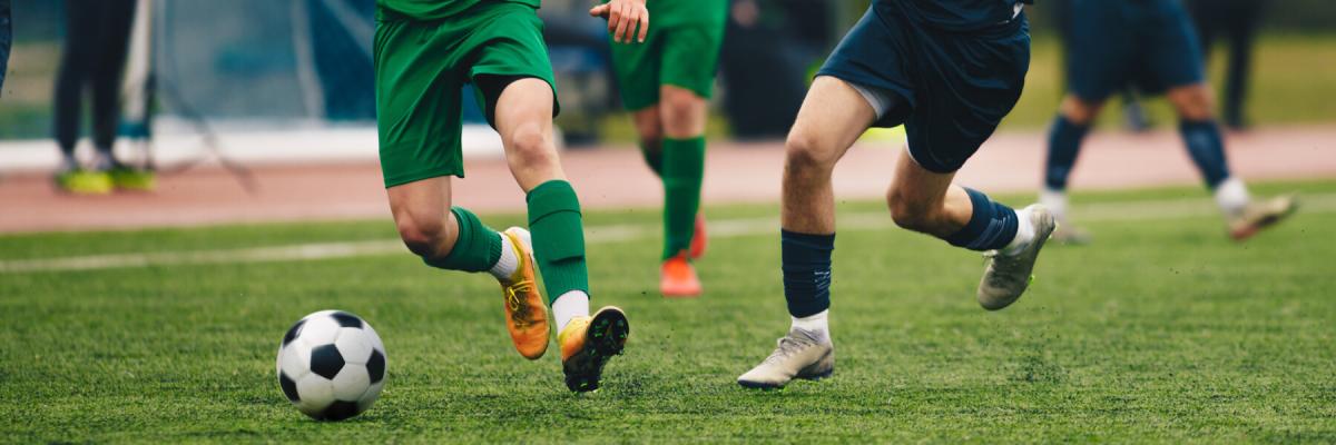 soccer game between two teams, closeup of two players going for the ball, athletes running and kicking soccer ball